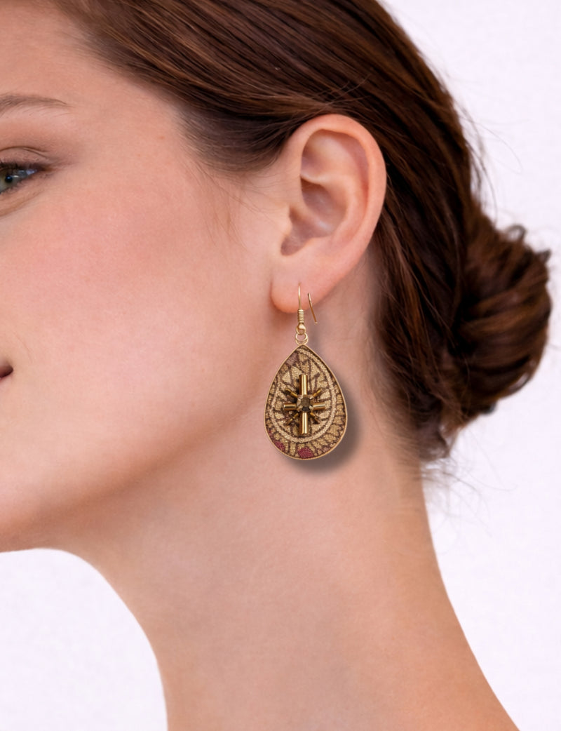 Beige tropical teardrop earrings with gold-tone cross and bead details worn by a woman in side profile view