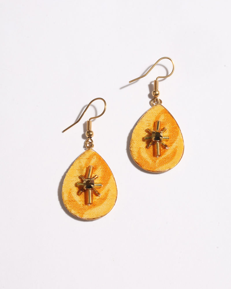 Yellow teardrop-shaped earrings with gold-tone hooks and central beaded starburst embellishment, flat lay on white background