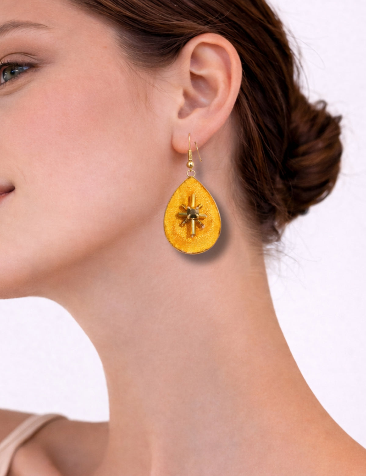 Yellow teardrop-shaped earrings with abstract gold bead design worn on a woman's ear, side view close-up