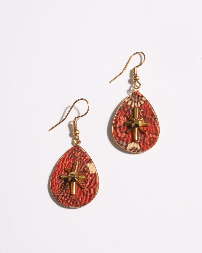 Orange tropical teardrop earrings with gold-tone hooks and beaded cross embellishment on fabric surface