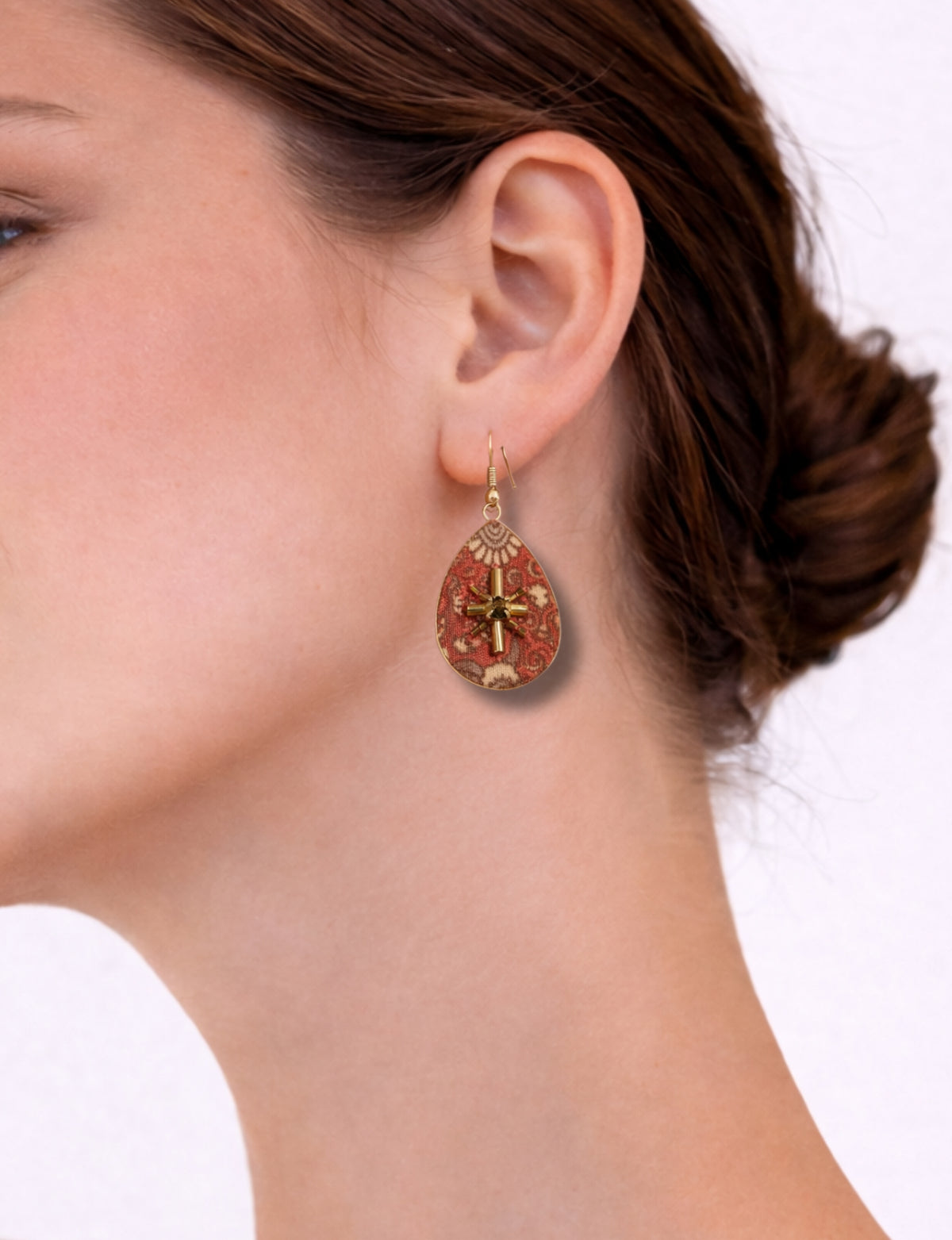 Woman wearing orange teardrop earrings with tropical floral pattern and gold cross detail, side view close-up