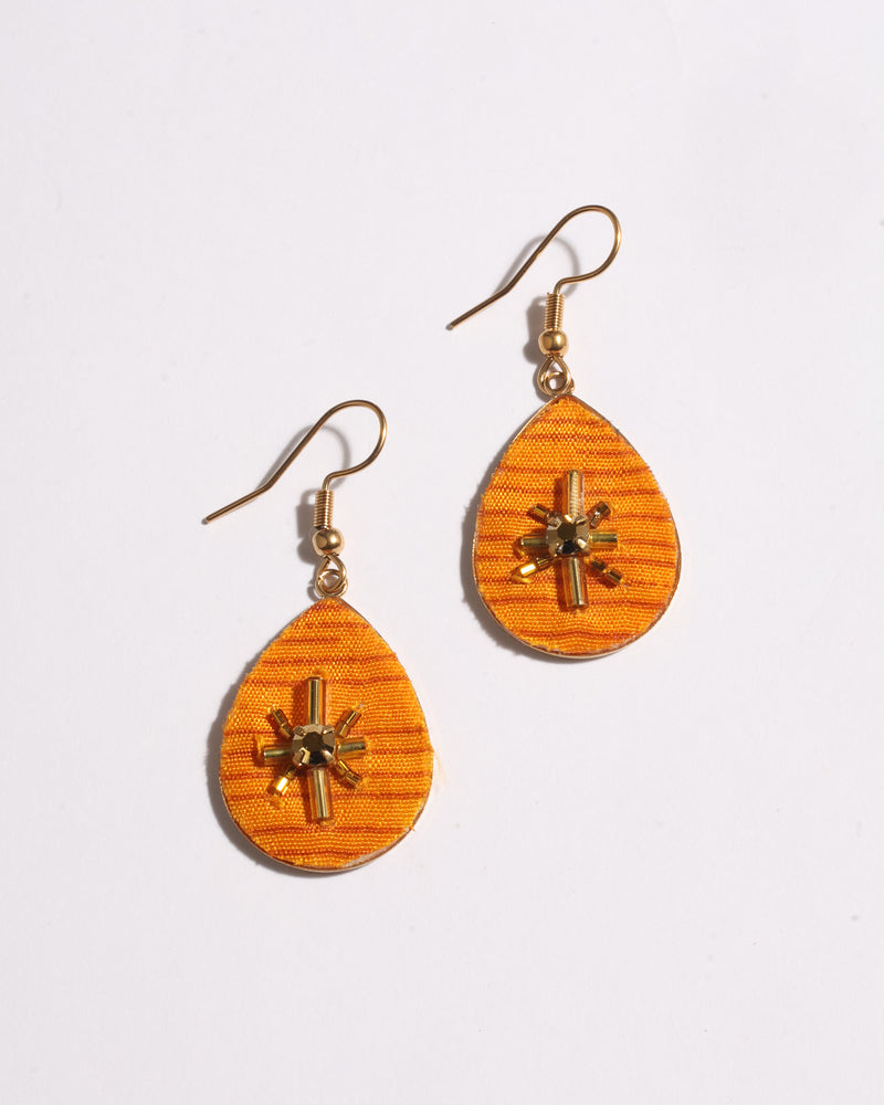Yellow teardrop-shaped earrings with gold-tone hooks and central bead and tube embellishments on fabric texture