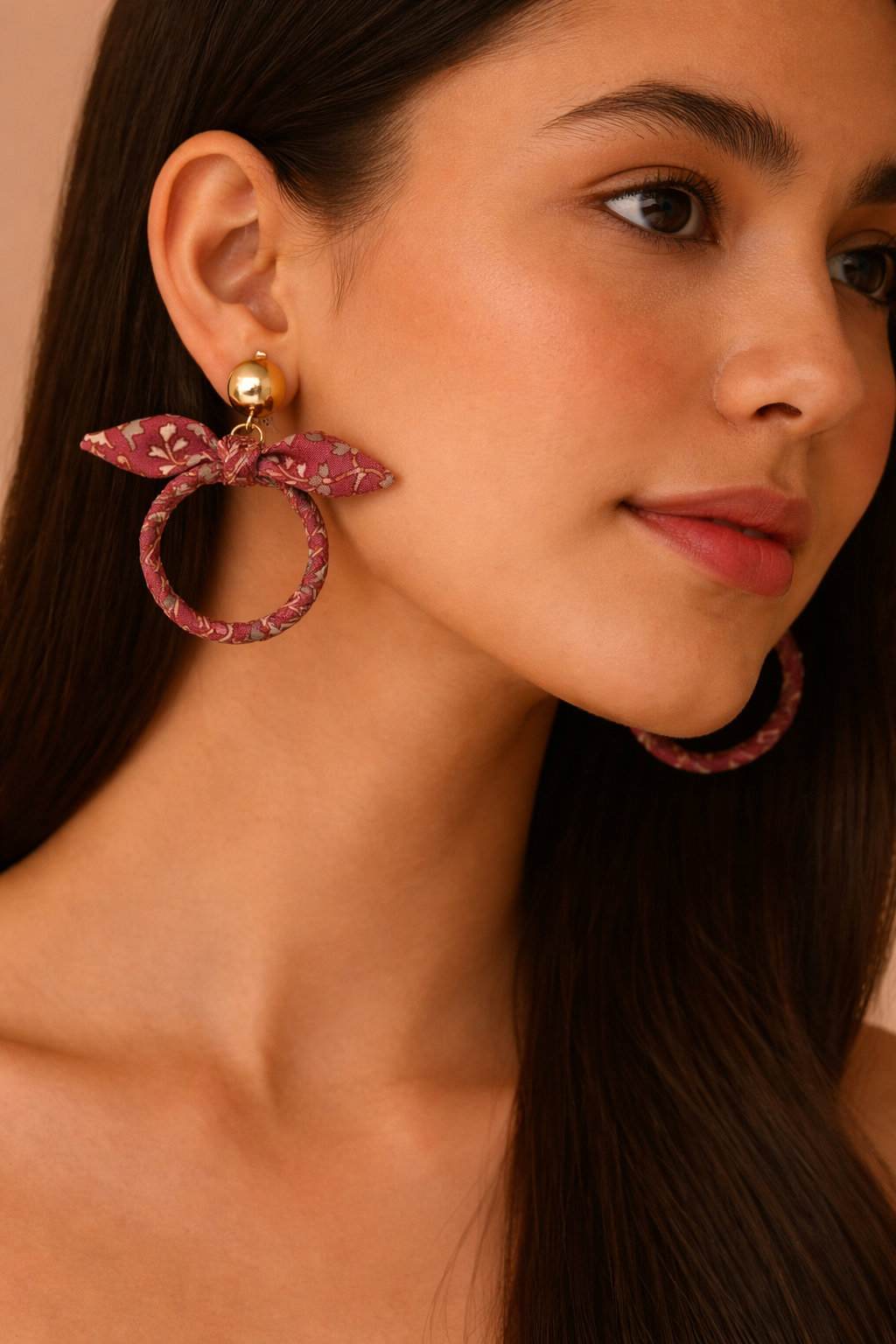 Model wearing pink tropical bow earrings with gold ball studs and fabric-wrapped hoop design, close-up side view