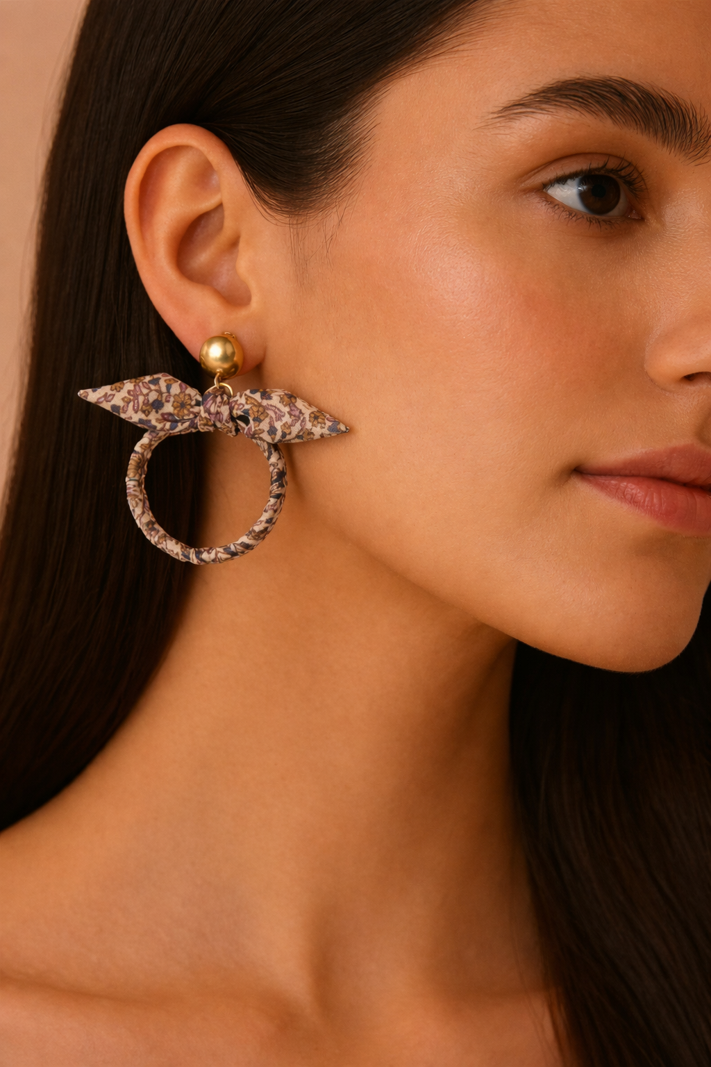 Beige tropical bow earrings with floral fabric wrapped hoop and gold-tone round stud worn by model in side view