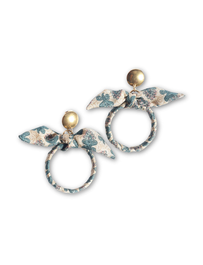 Beige tropical bow earrings with green floral print fabric wrapped around circular hoops and gold-tone round studs, flat lay