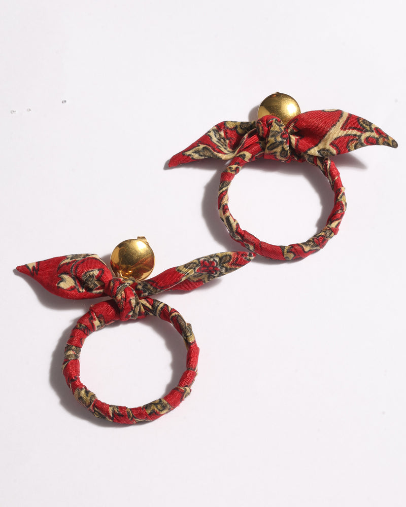 Pair of red tropical patterned fabric bow earrings with gold round studs, shown flat on white background