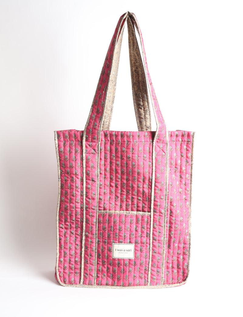 Quilted carry-all tote bag with a structured rectangular shape, long shoulder straps, and an external patch pocket.