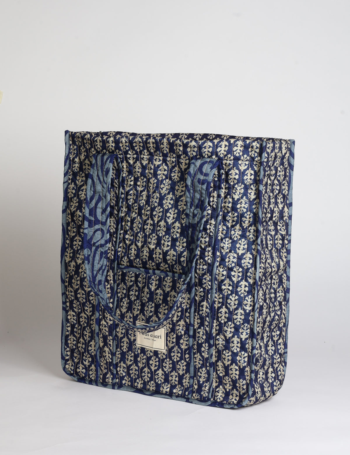 Quilted carry-all tote bag with long shoulder straps, flat base, and external patch pocket.