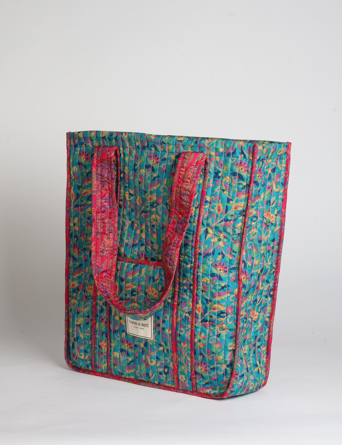 Quilted carry-all tote bag with long shoulder straps, flat base, and external patch pocket.