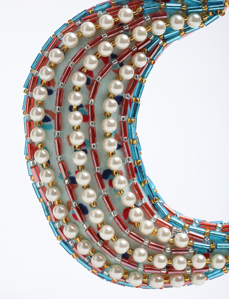Crescent moon ornament decorated with white pearls, red and blue cylindrical beads on a patterned fabric base