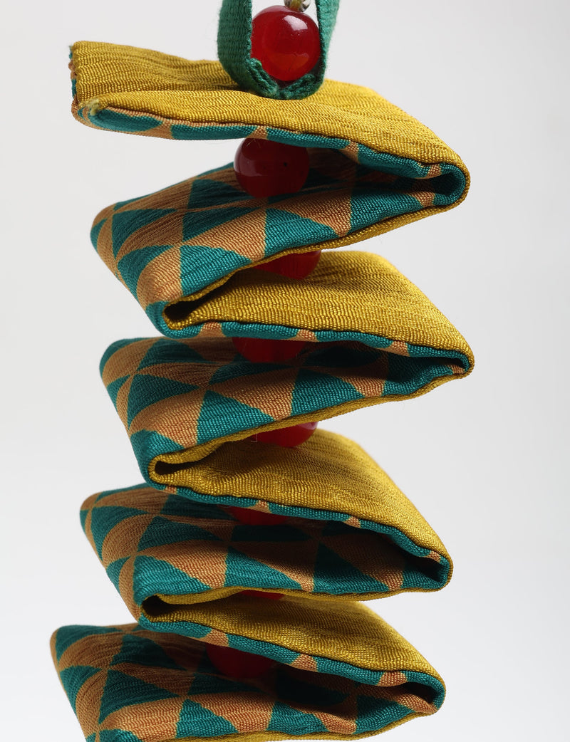 Spiral fabric ornament with mustard yellow and teal geometric pattern and red beads, close-up front view on white background