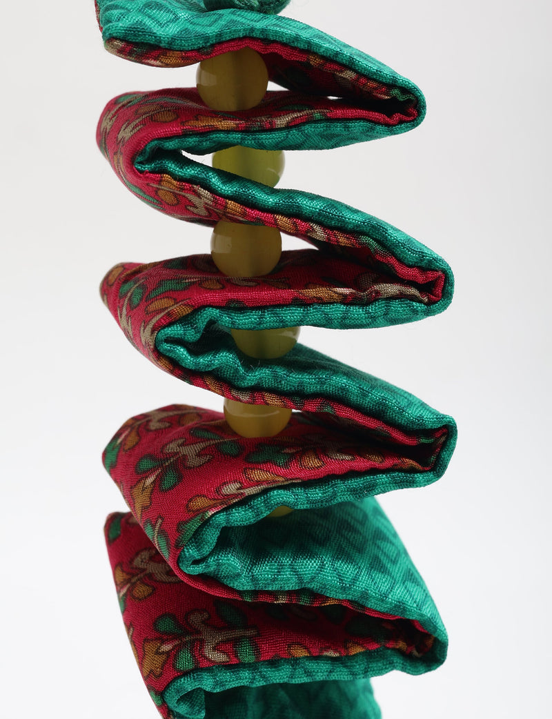 Close-up of a twisted fabric candy cane ornament with red and green patterned cloth and yellow beads threaded inside