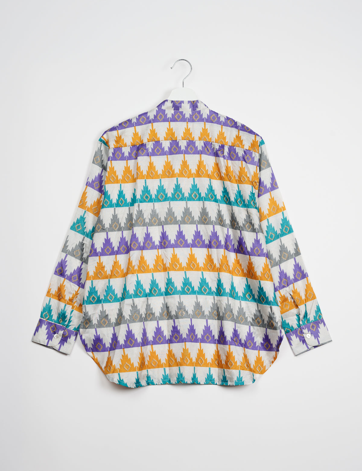 Longline shirt with white base and geometric pattern in purple, orange, teal, and gray, shown from back on hanger