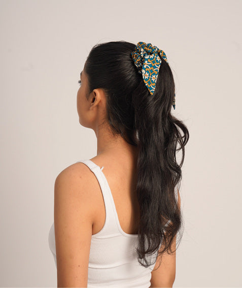 Woman wearing a blue and orange tropical patterned scrunchy holding long black hair in a ponytail, side back view