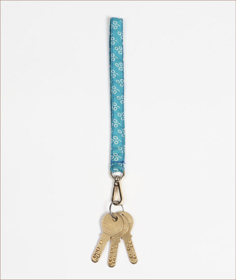 Blue fabric keychain lanyard with white circular pattern and metal clip holding three brass keys, flat lay on white background