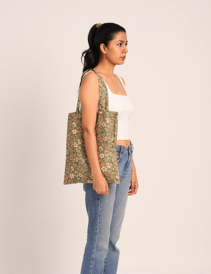 Woman wearing a green floral print ethnic shopper bag over shoulder, paired with white tank top and blue jeans, side view