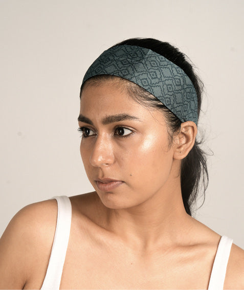 Model wearing a wide dark green headband with a geometric pattern, styled with a white tank top, front side view