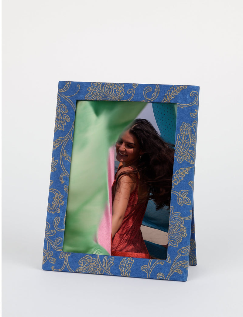 Blue photo frame with gold floral geometric pattern, standing upright with a photo of a smiling woman in a red dress inside