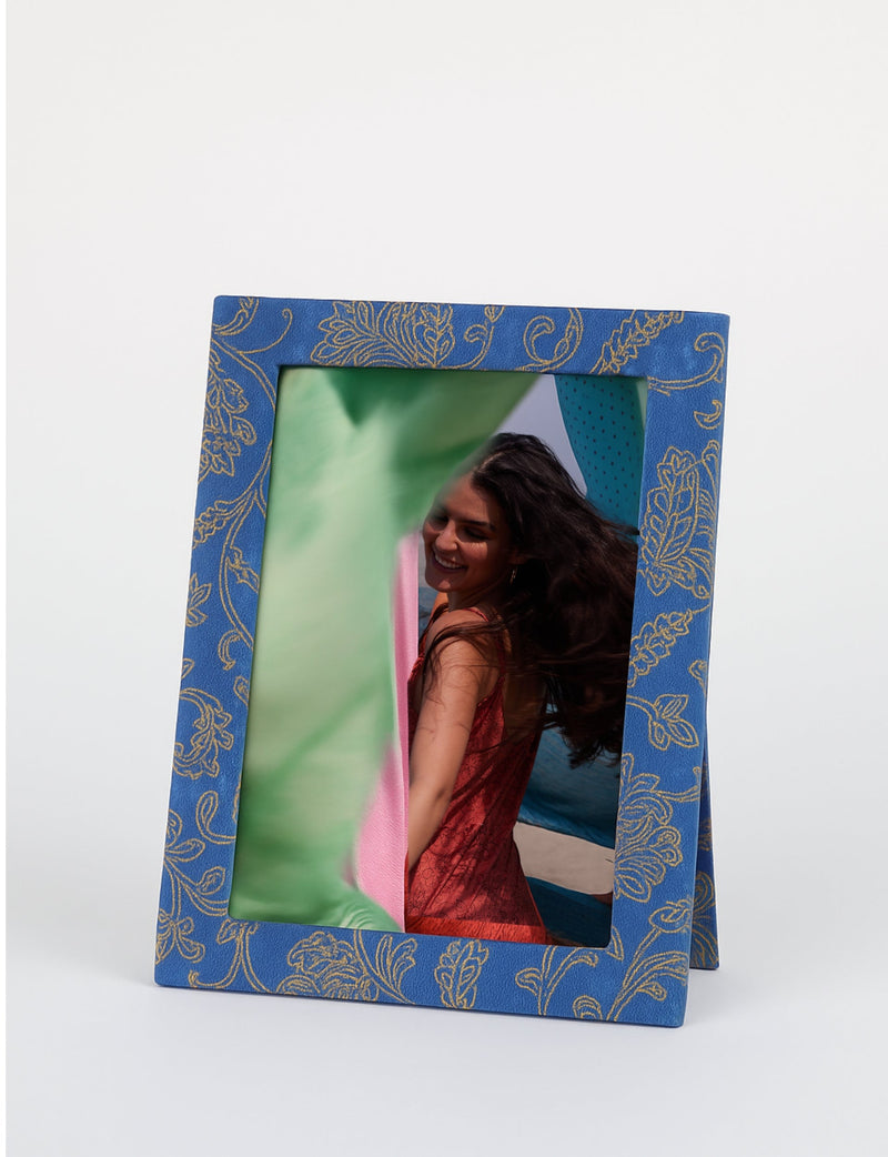 Blue photo frame with gold floral pattern, standing, holding a photo of a woman in a red dress with flowing hair outdoors
