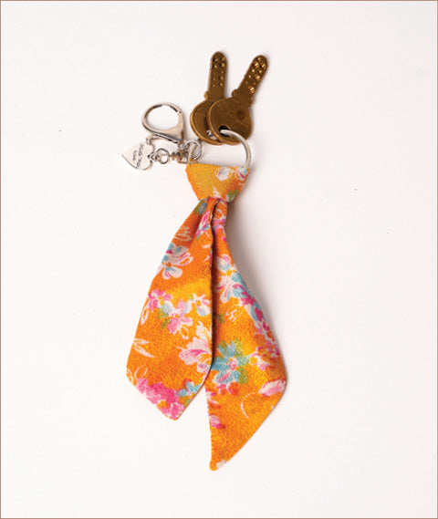 Keychain with orange floral fabric tie, silver ring, lobster clasp, and two brass keys on white background