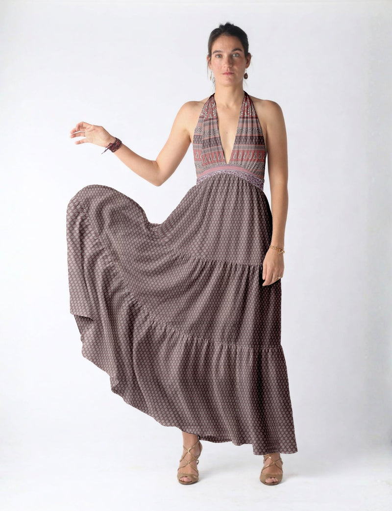 Woman wearing a purple maxi tiered dress with a deep V neckline and micro geometric pattern, standing against a white