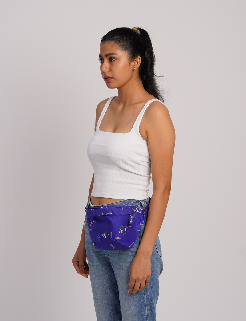 Woman wearing a blue abstract midi belt bag with floral pattern, paired with white tank top and blue jeans, side view