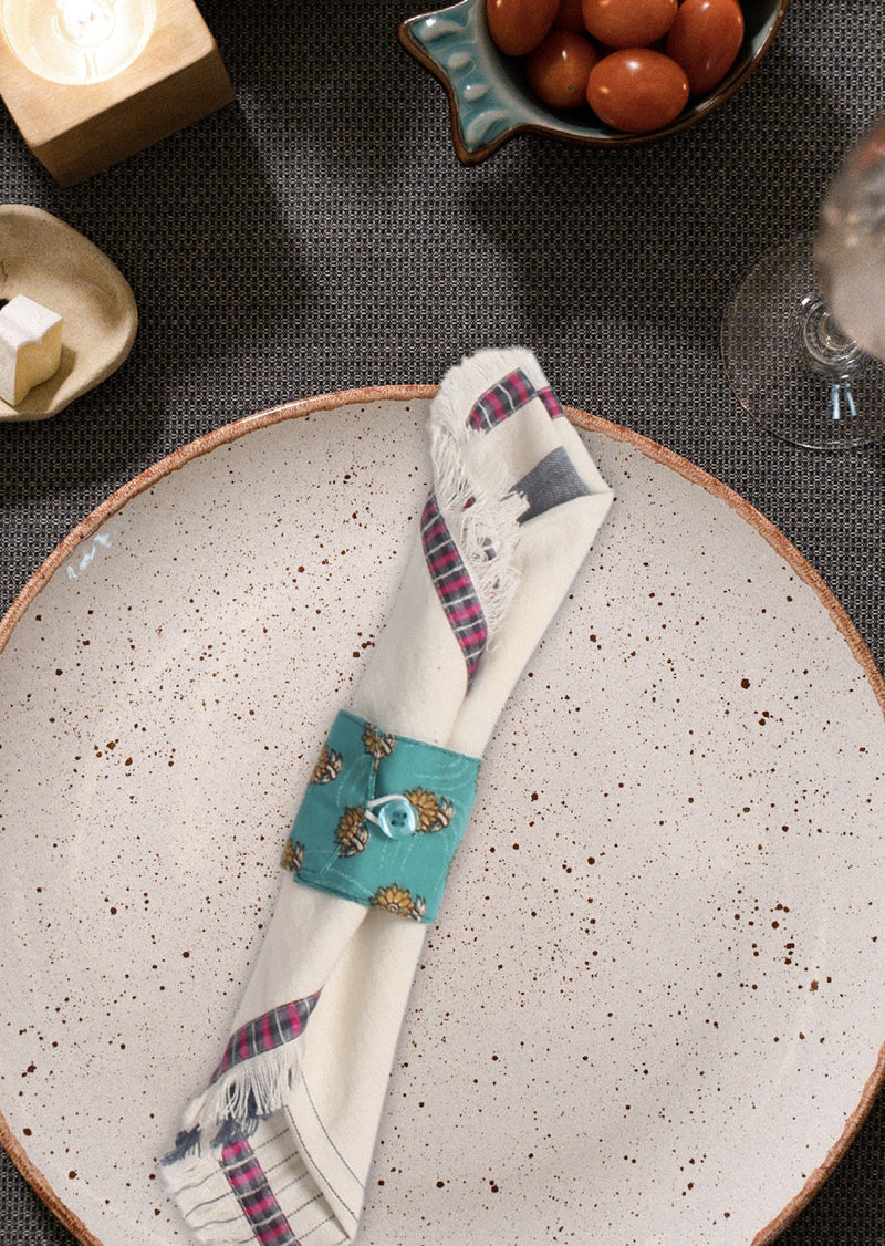 Set of six brown napkin rings with micro floral design, shown on a folded cream napkin with plaid edges on a speckled plate