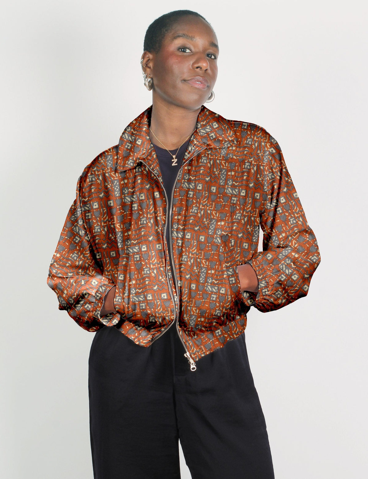 Woman wearing an orange bomber jacket with Indian ethnic geometric patterns, front zipper, and side pockets, paired with