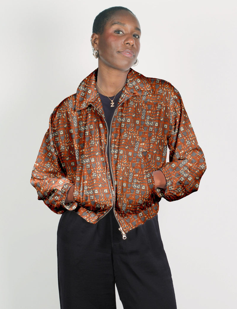 Woman wearing an orange bomber jacket with Indian ethnic geometric patterns, front zipper, and side pockets, paired with
