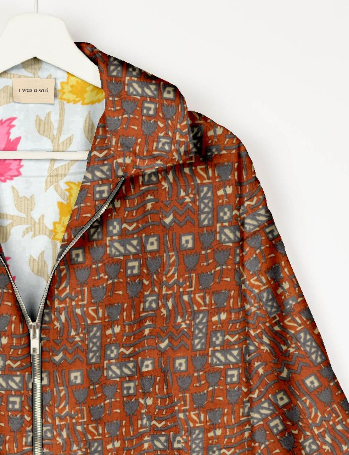 Orange bomber jacket with gray geometric and floral ethnic print, silver zipper, and inner floral lining on white hanger