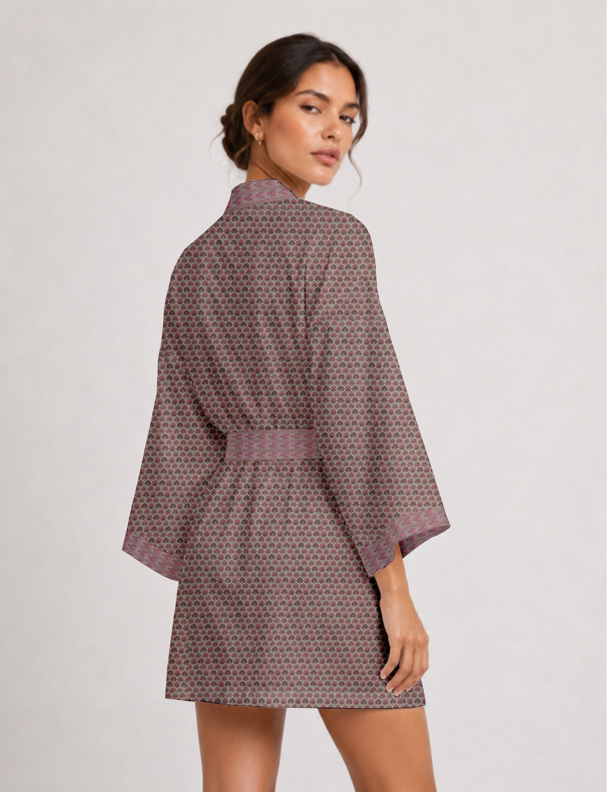 Woman wearing short kimono robe with pink and gray small floral pattern and geometric trim on sleeves and belt, back view