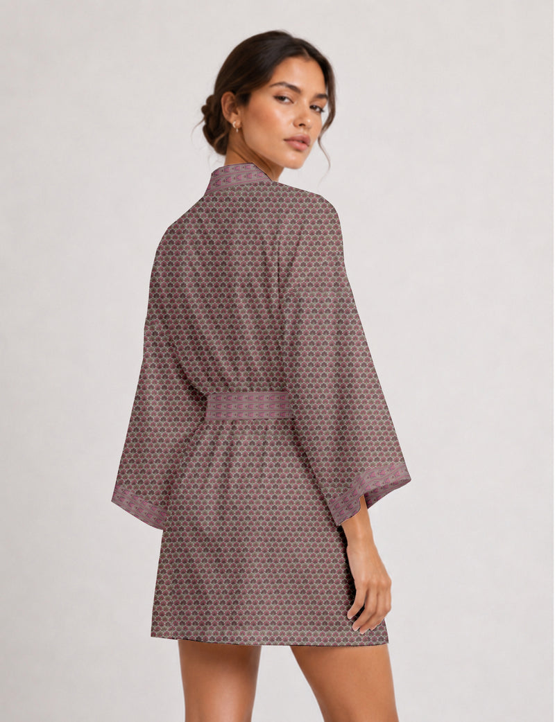 Woman wearing short kimono robe with pink and gray small floral pattern and geometric trim on sleeves and belt, back view