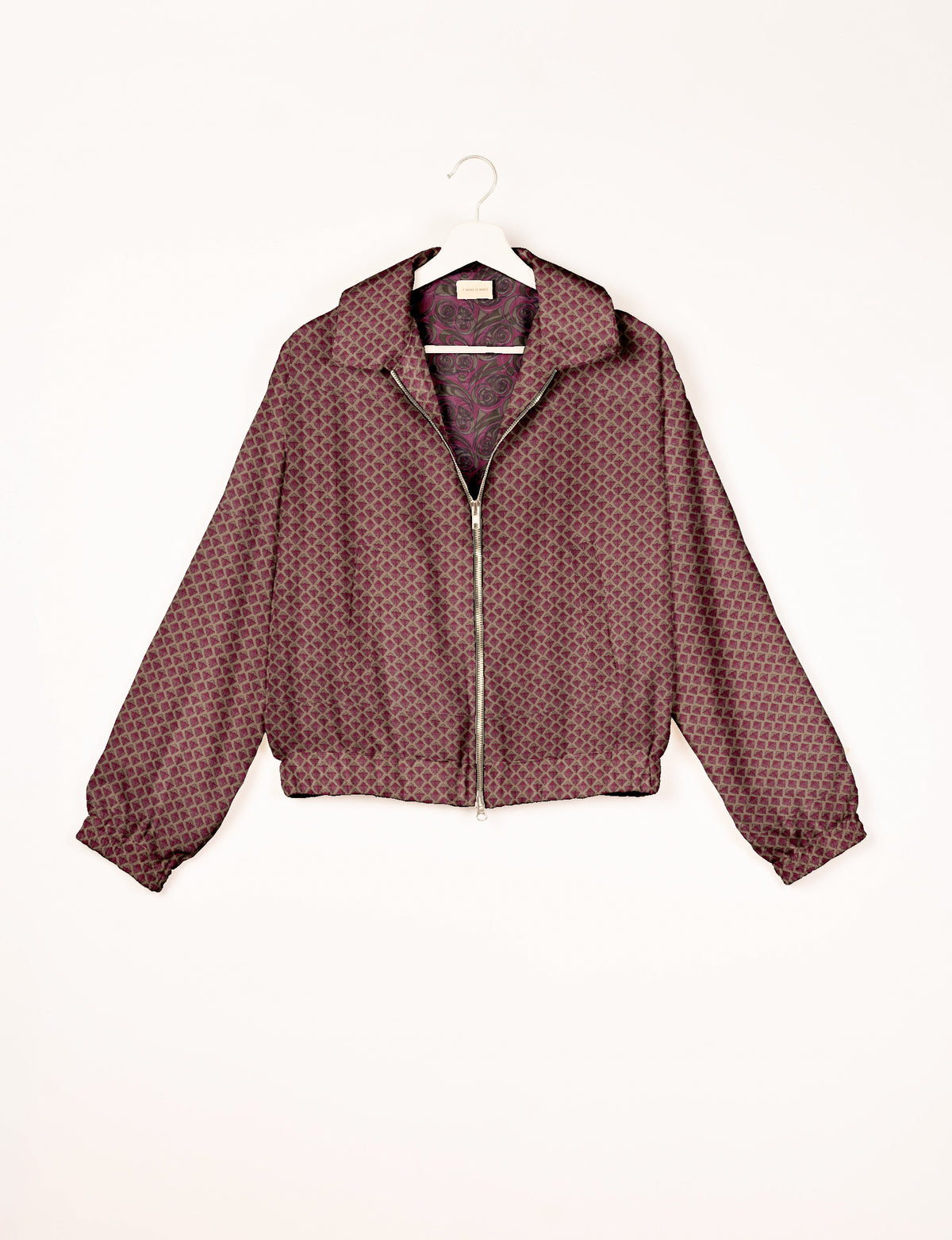 Pink bomber jacket with geometric diamond pattern, front zipper, collar, elastic cuffs, and floral inner lining, hanging on