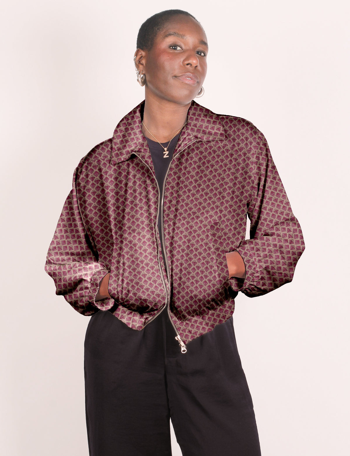 Woman wearing a pink geometric patterned bomber jacket with a front zipper and elastic cuffs, paired with black pants