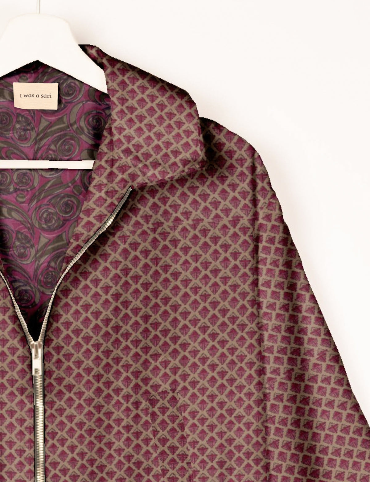 Pink and brown geometric patterned bomber jacket with silver zipper, shown on hanger with patterned inner lining and label