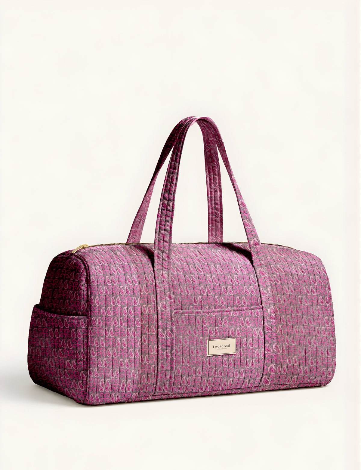 Woman holding a brown paisley quilted barrel bag with front zipper pocket, wearing light blue jeans and white sneakers