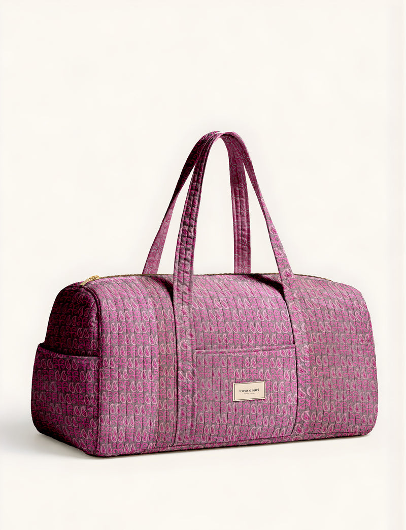 Woman holding a brown paisley quilted barrel bag with front zipper pocket, wearing light blue jeans and white sneakers