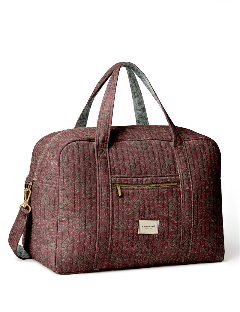 Brown quilted duffle bag with paisley pattern, front zip pocket, dual handles, and label reading "I was a sari"