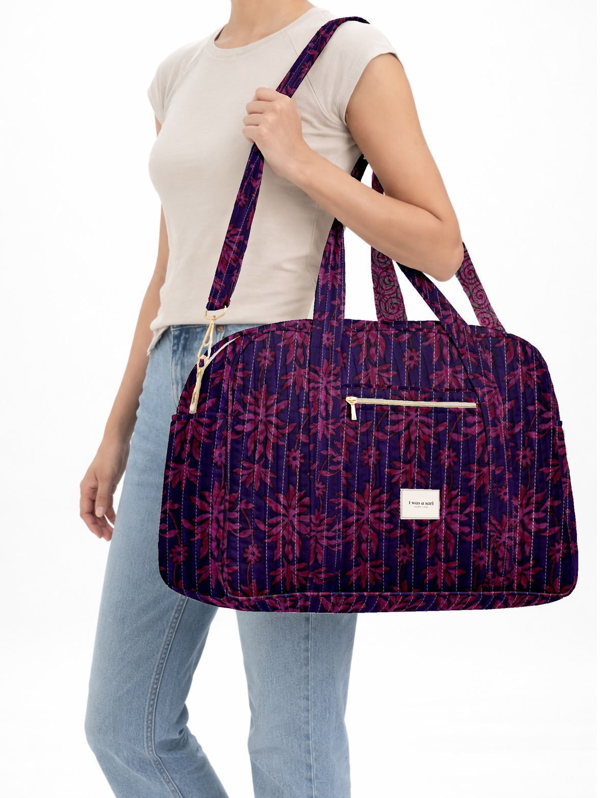 Woman wearing a quilted duffle bag with purple and pink leaf pattern, front zip pocket, and dual handles over shoulder