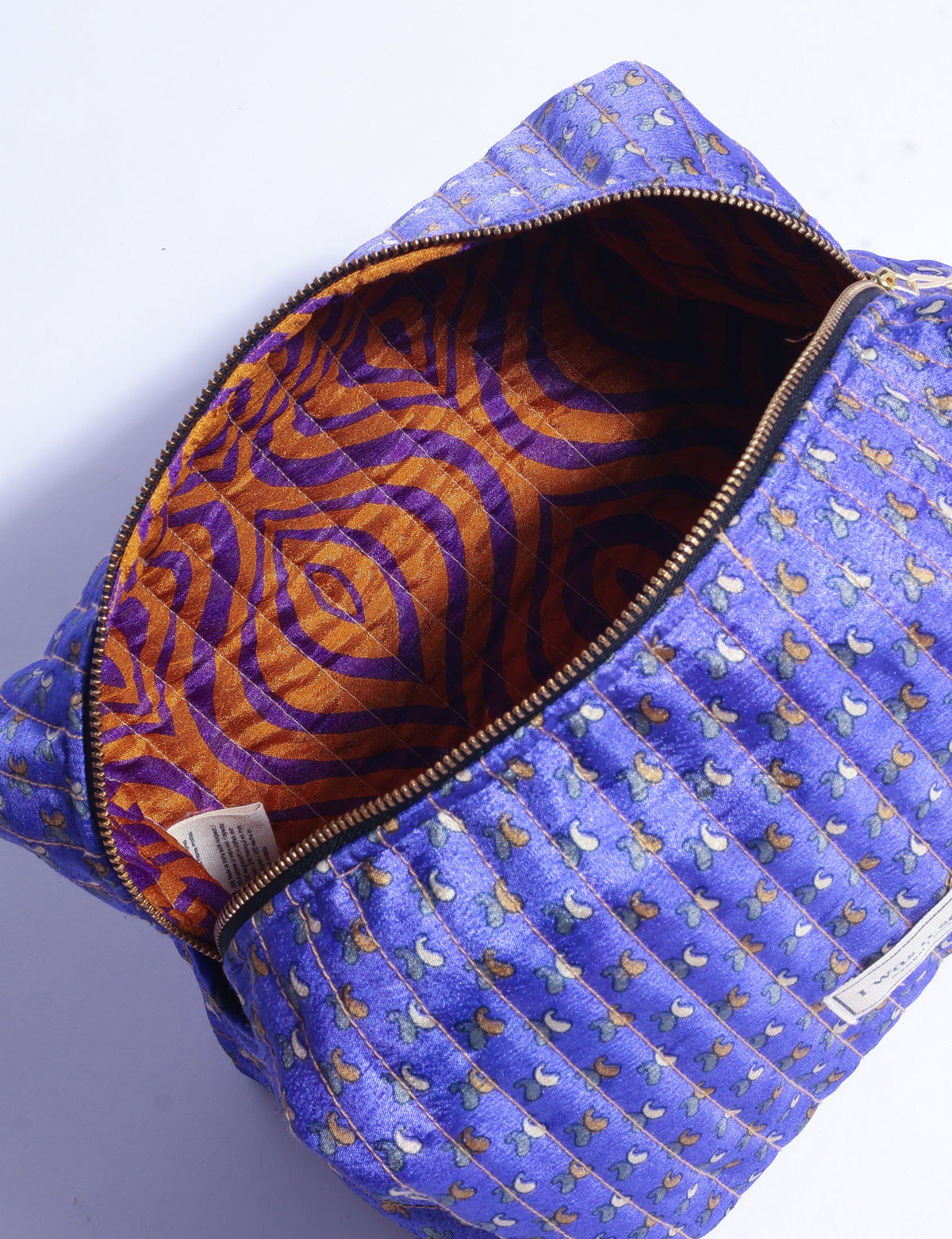 Quilted purple utility pouch with micro floral design, gold zipper, and orange and purple patterned interior, open top view