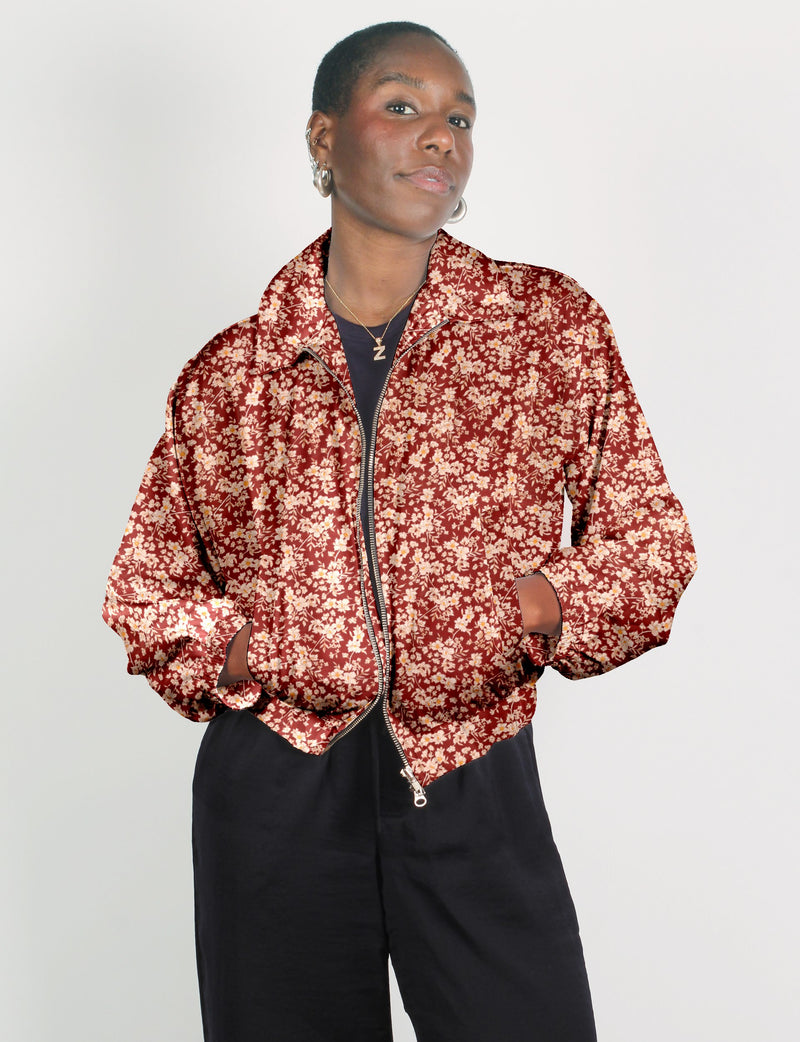 Person wearing a red floral bomber jacket with a front zipper and pockets, paired with black pants, front view