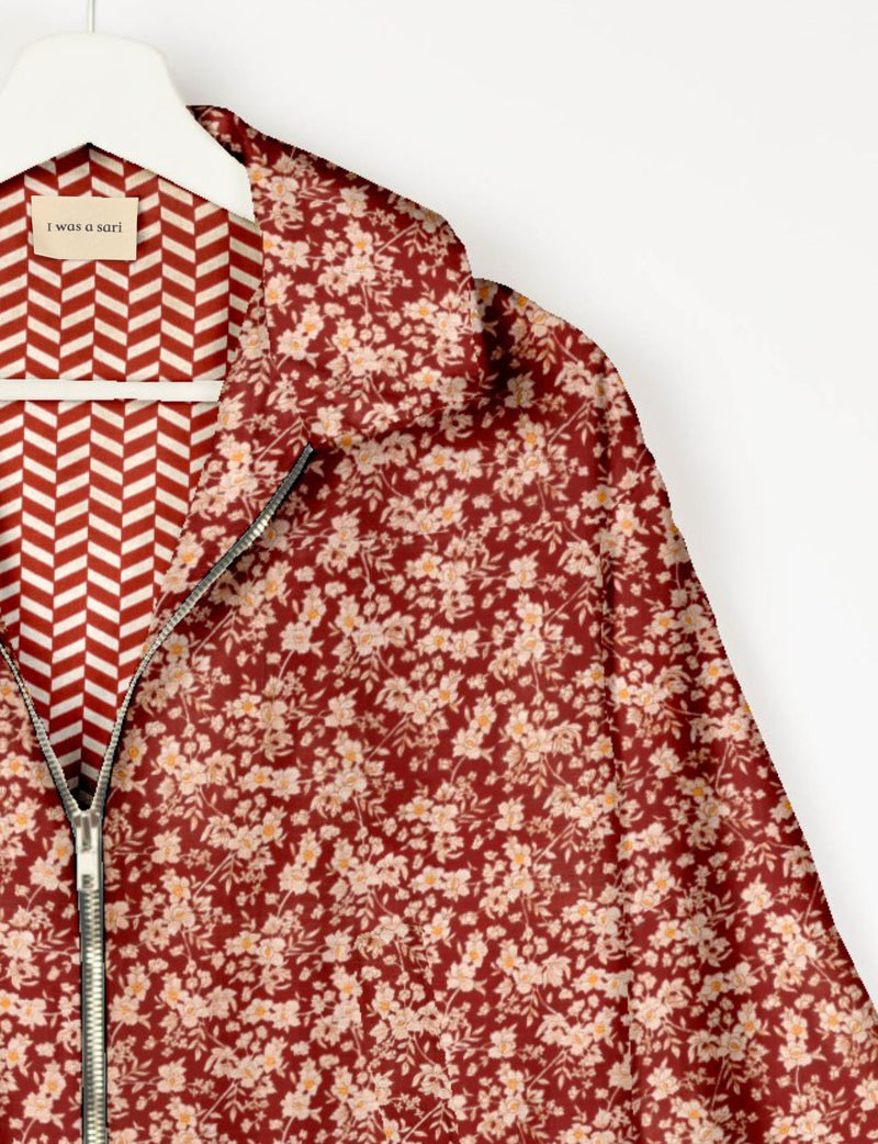 Red floral bomber jacket with silver zipper, hanging on white hanger with patterned lining and label reading "I was a sari"