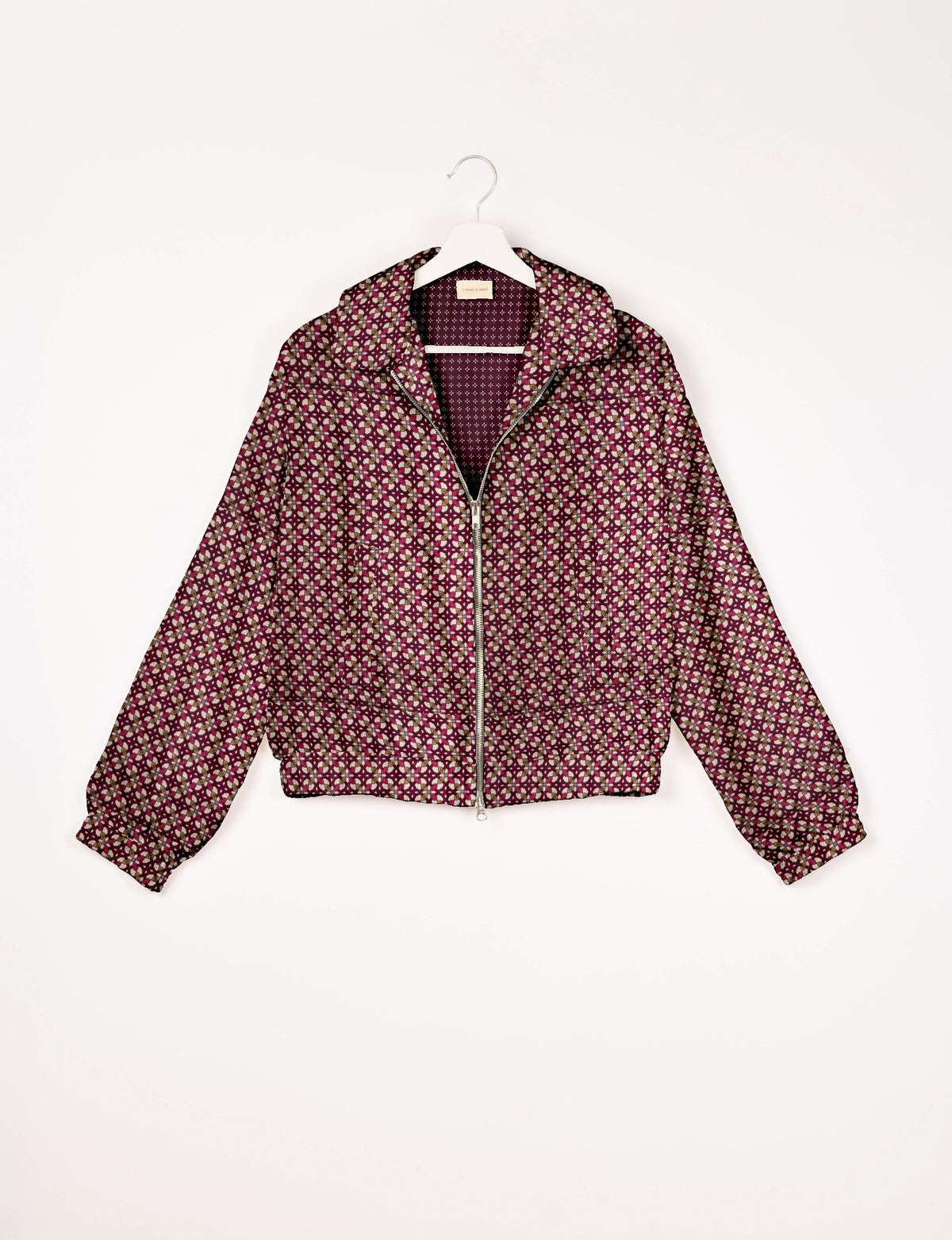 Red bomber jacket with geometric pattern, front zipper, collar, and elastic cuffs, hanging on white hanger