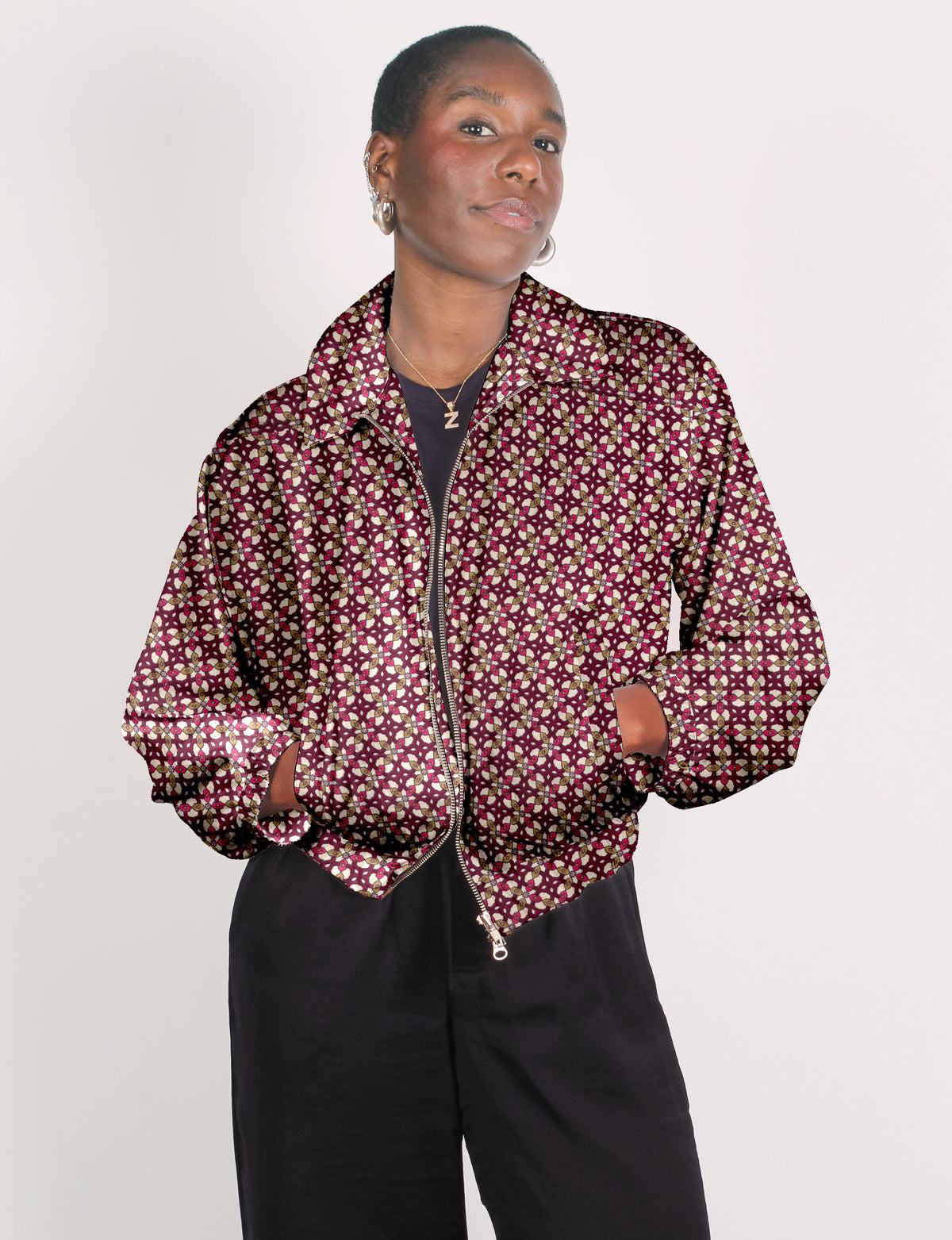 Model wearing a red geometric patterned bomber jacket with a front zipper and collar, paired with black pants