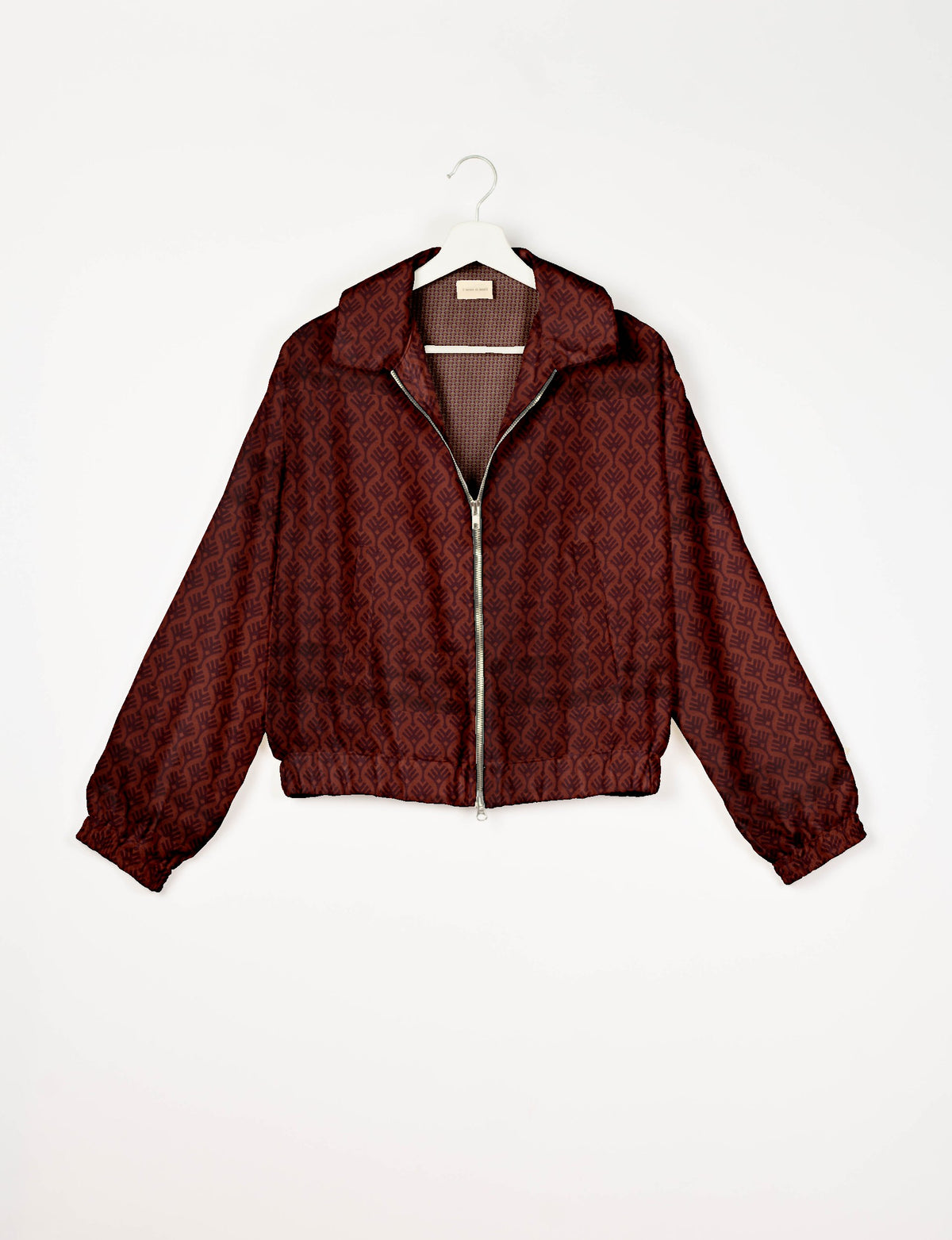 Red bomber jacket with dark red leaf pattern, front zipper, elastic cuffs and hem, hanging on white hanger front view