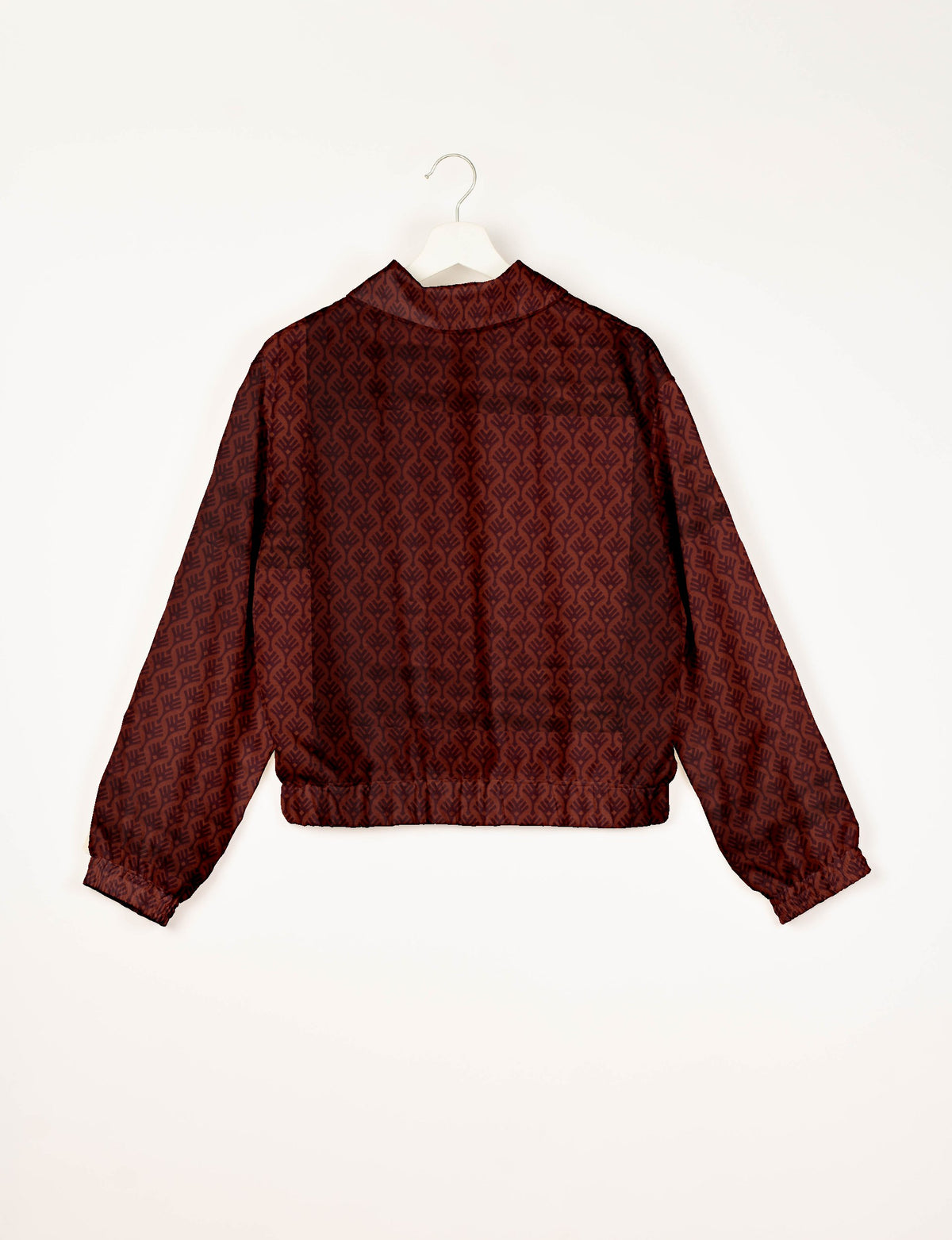 Red bomber jacket with dark leaf pattern, elastic cuffs and waistband, shown from back on white hanger