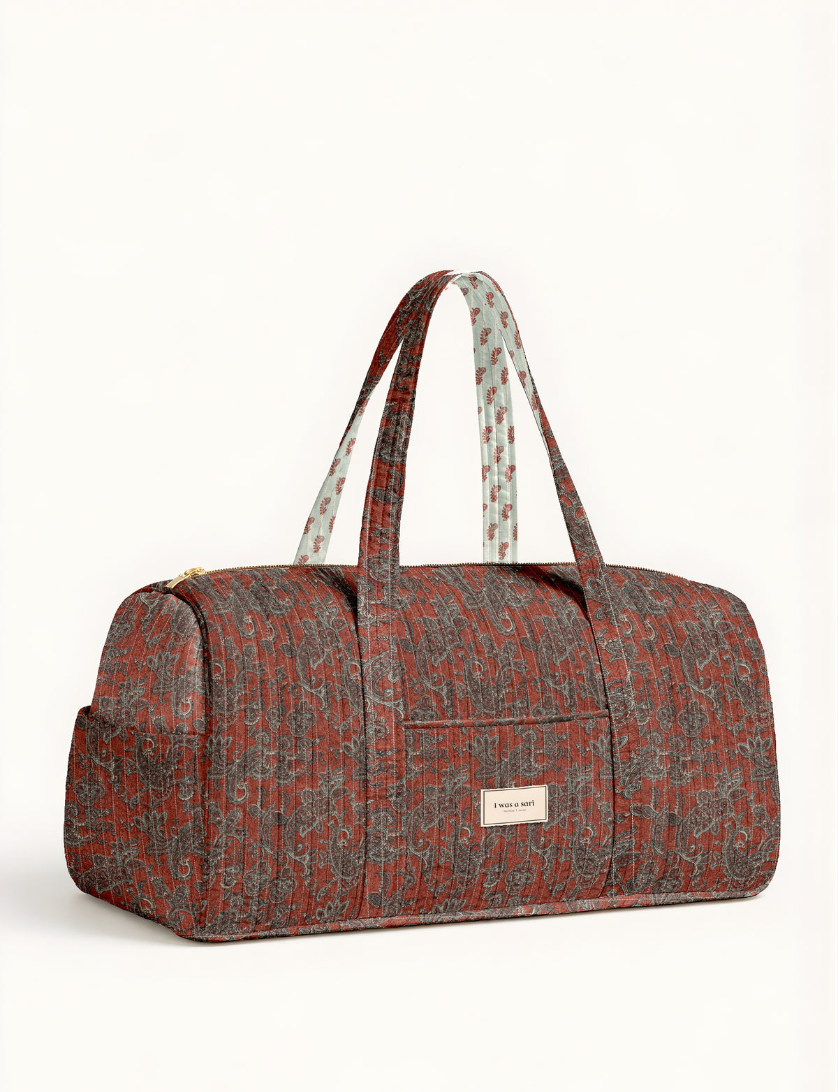 Quilted barrel bag in red paisley pattern with dual handles and front label reading "I was a sari" shown from front angle