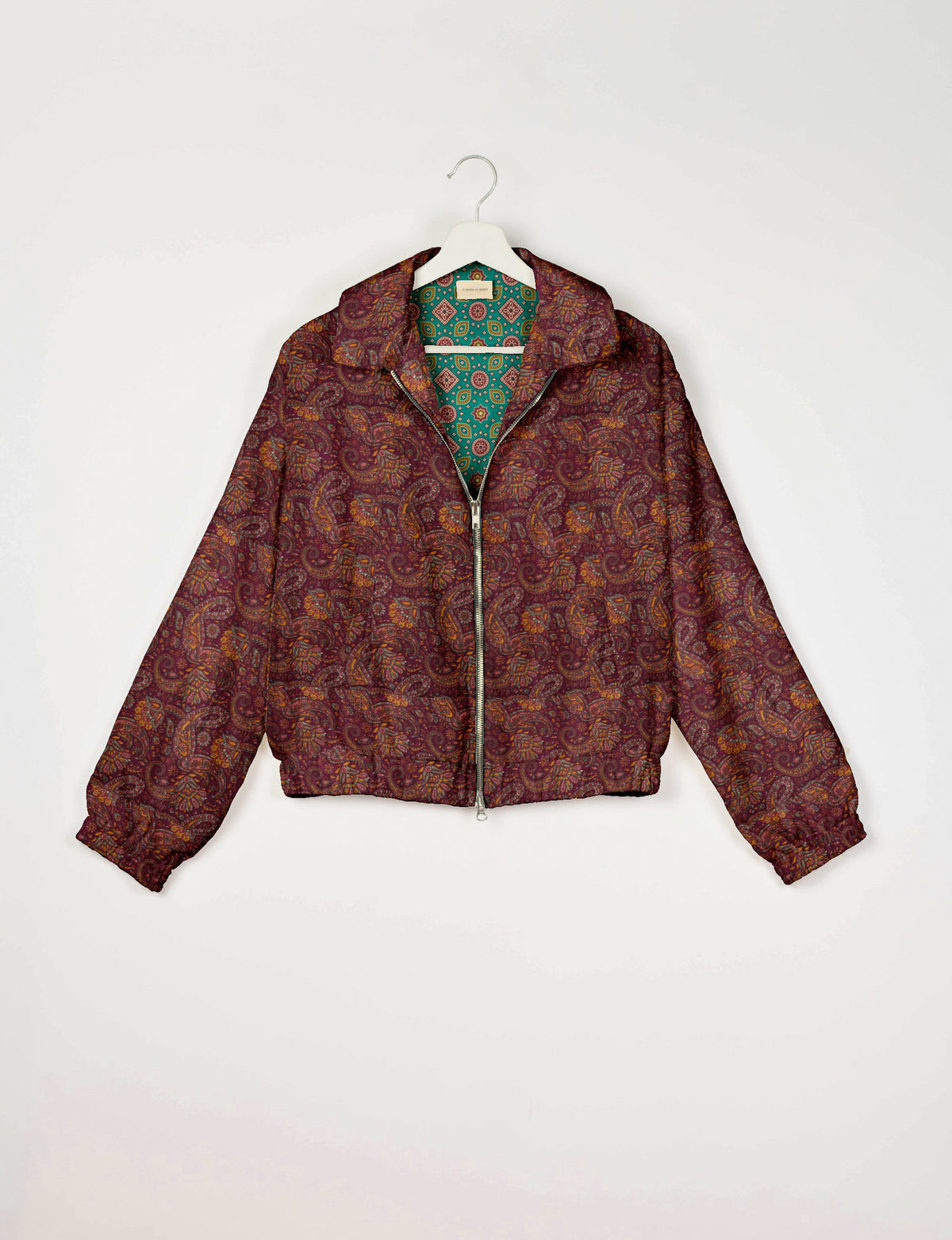 Red paisley bomber jacket with front zipper, elastic cuffs and waistband, shown hanging with green patterned lining visible