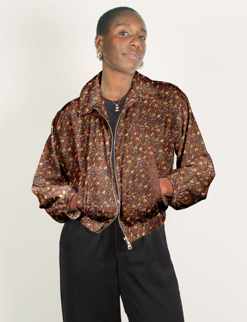 Woman wearing a red floral patterned bomber jacket with a front zipper and elastic cuffs, paired with black pants