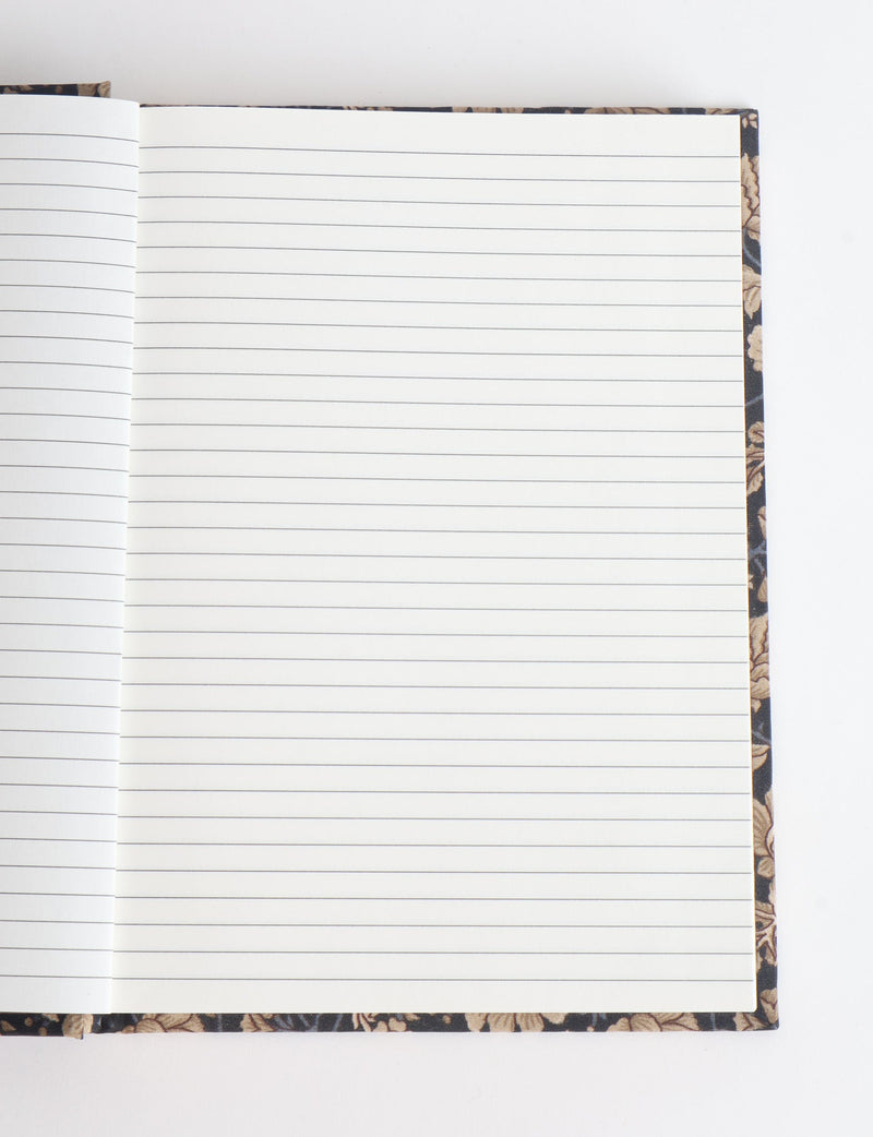 Open notebook with lined white pages and a dark floral-patterned hard cover visible at edges, flat lay view